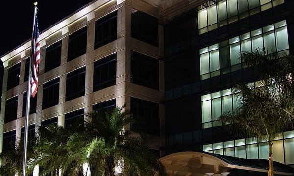 A four-story office building illuminated by landscape lighting at night, with an American flag and palm trees in front