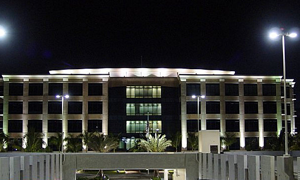 Modern office building illuminated at night, with landscape lighting enhancing the well-lit facade and palm trees in front