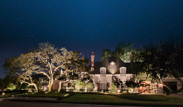 Luxury home with landscape lighting that illuminates the large oak trees and covers the home in well-designed lighting patterns