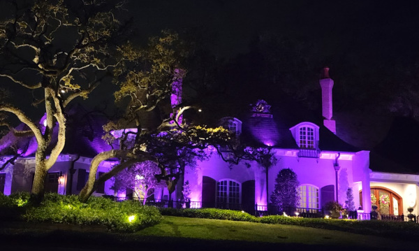 Stately European styled mansion illuminated with vibrant purple landscape lighting